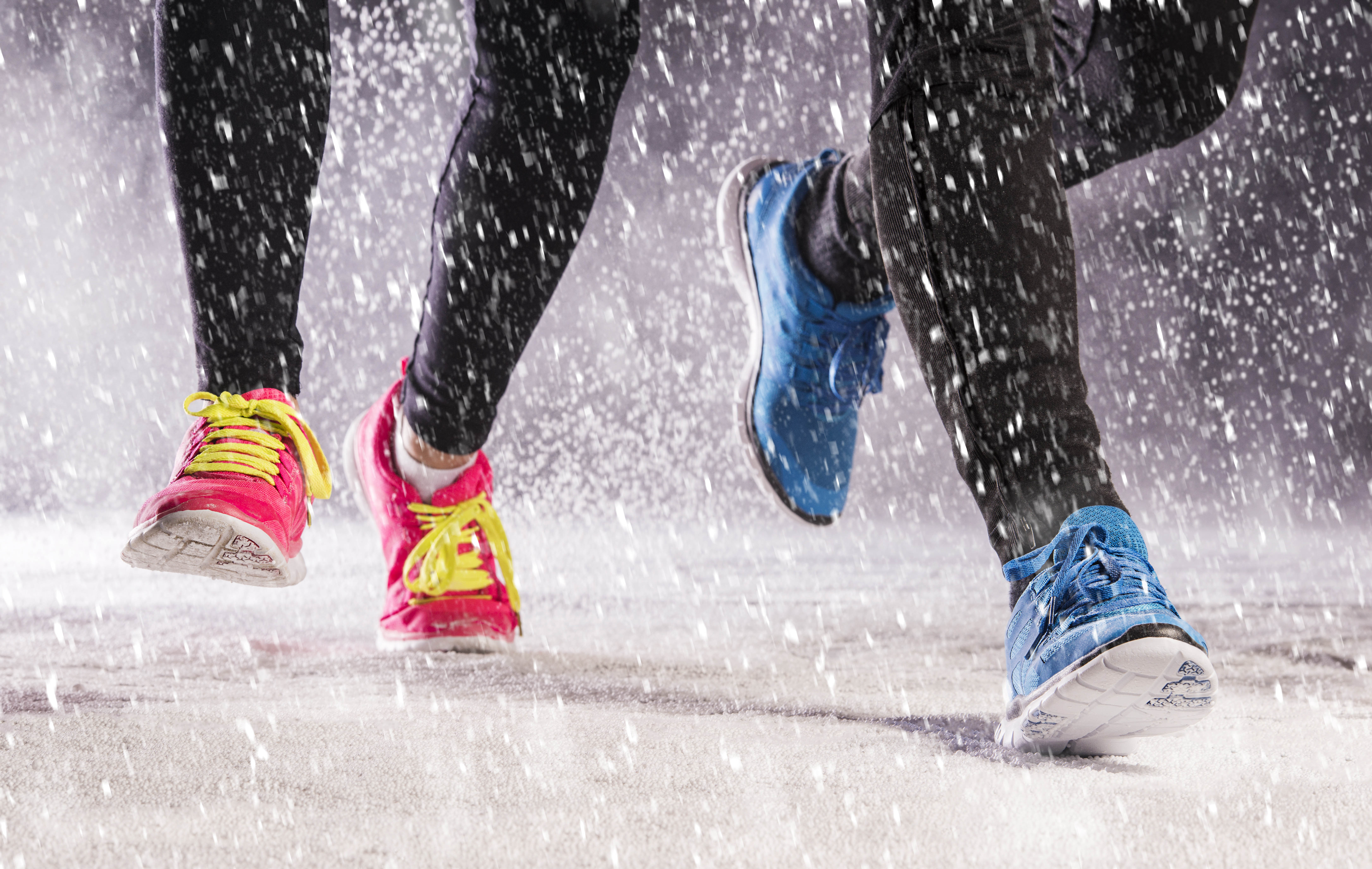 Close-up of two sets of feet running in the snow